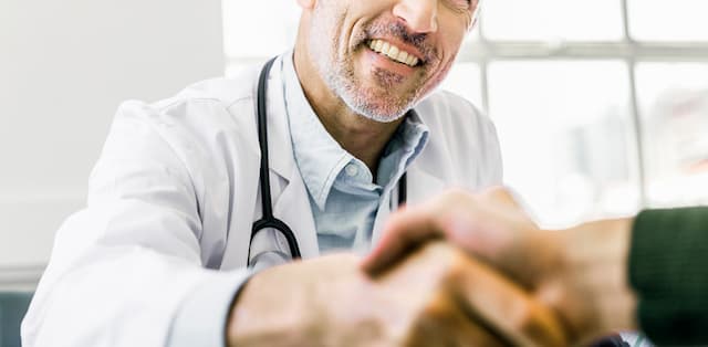 Man in white lab coat is smiling and shaking hands with a person out of frame