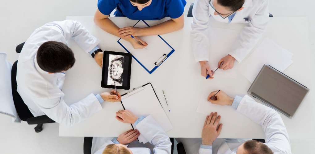 A team of dentists sit around a table looking at a patient dental record and discussing the case.