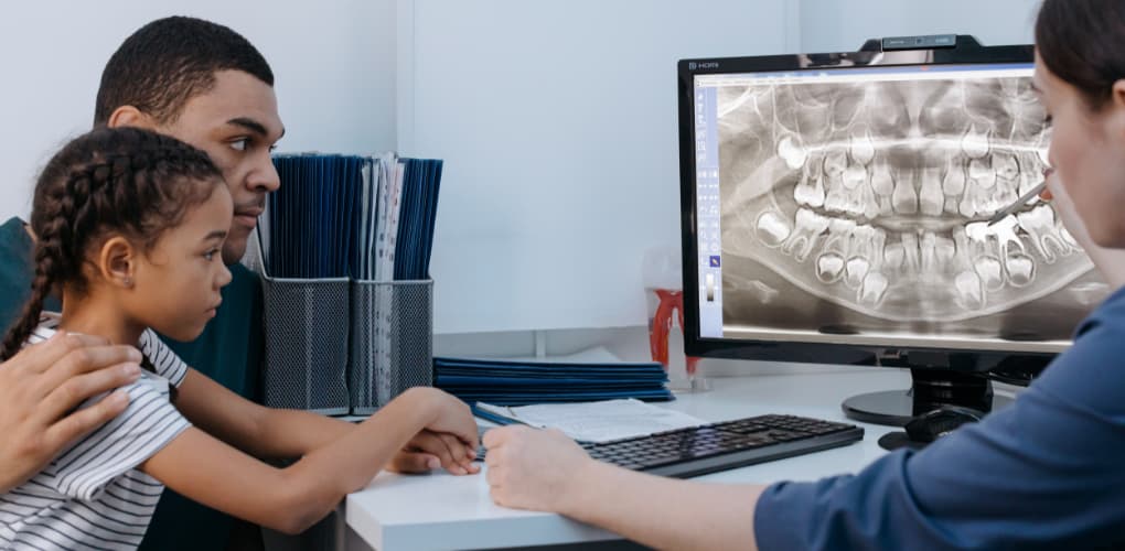 Father, child and dentist look at children's teeth xrays on the computer.