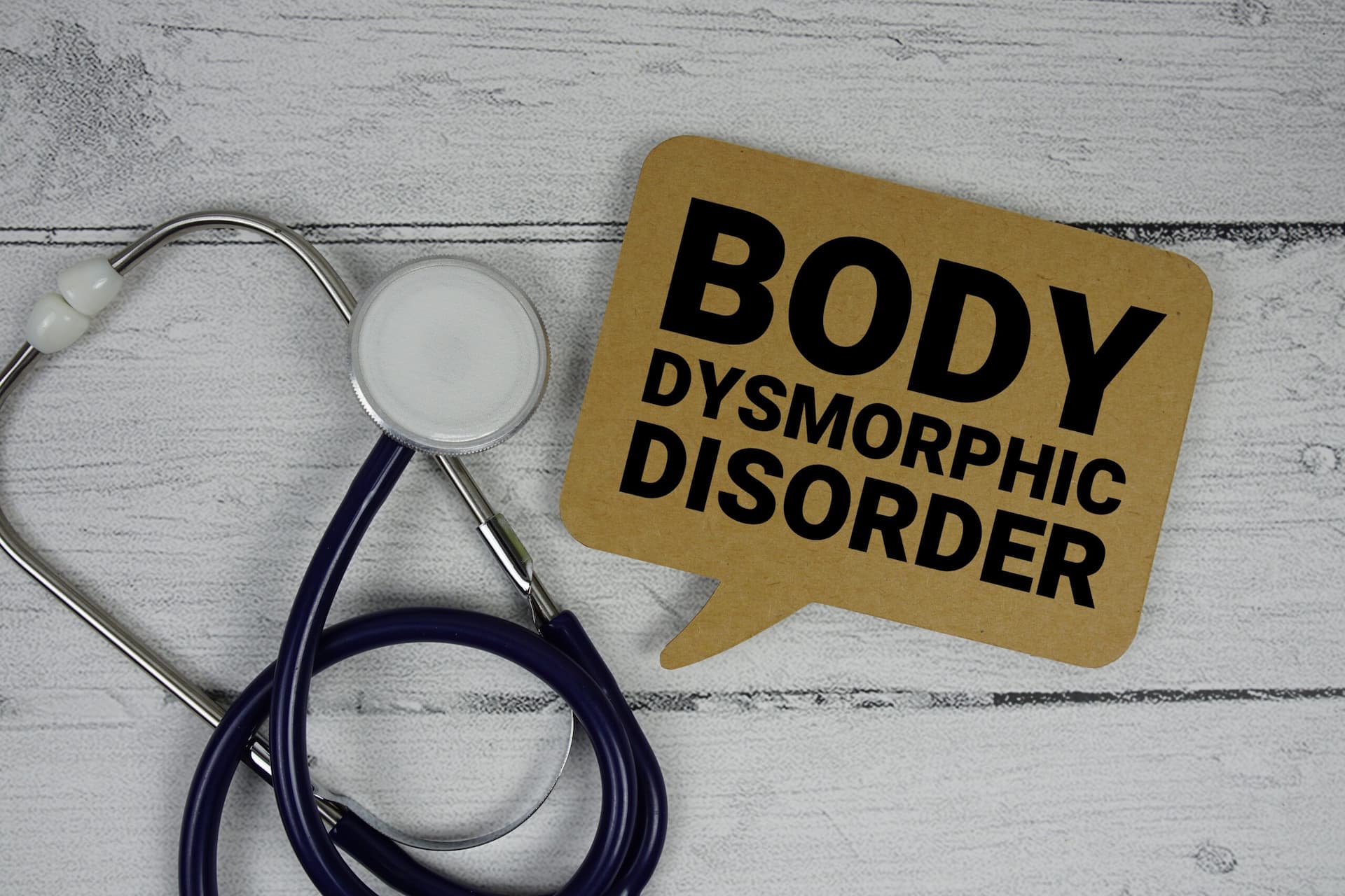 stethoscope on a table with a brown sign beside it displaying "Body Dysmorphic Disorder" in black letters