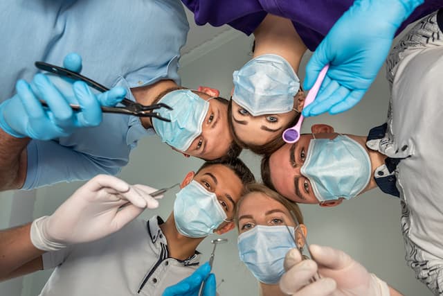 Group of young dentists wearing masks and gloves, holding dental instruments, looking down at the patient’s perspective.
