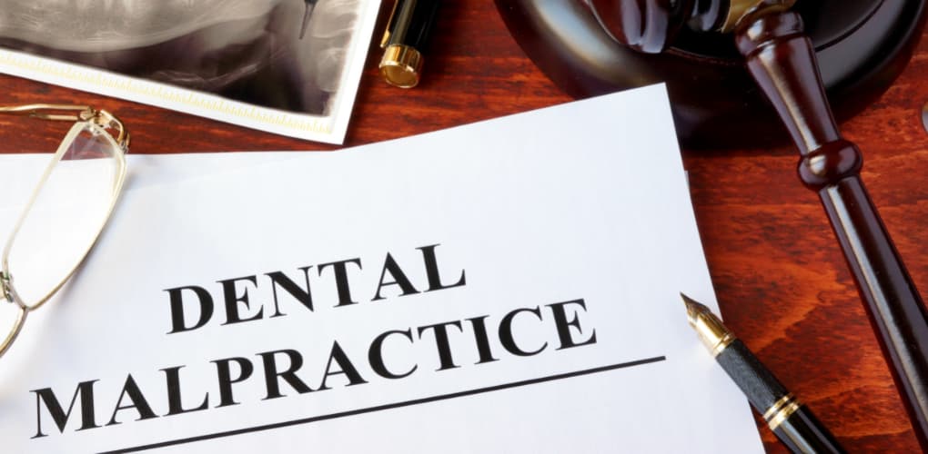 A pile of papers labeled "Dental Malpractice" sits on a desk next to a judge's gavel.