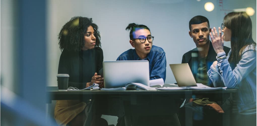 A group of dental students sit in a conference room around laptops, in discussion.