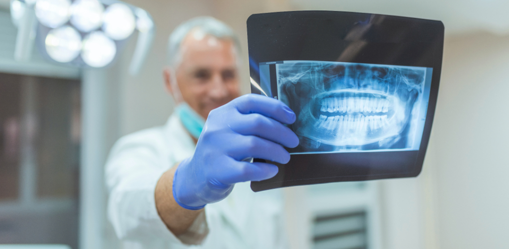 A male dentist smiles while holding up and examining a dental radiograph.