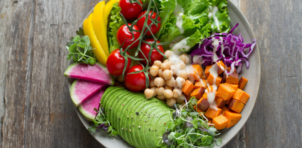 A vegan bowl with avocado, tomato, sweet potato, garbanzo beans and more on a table.